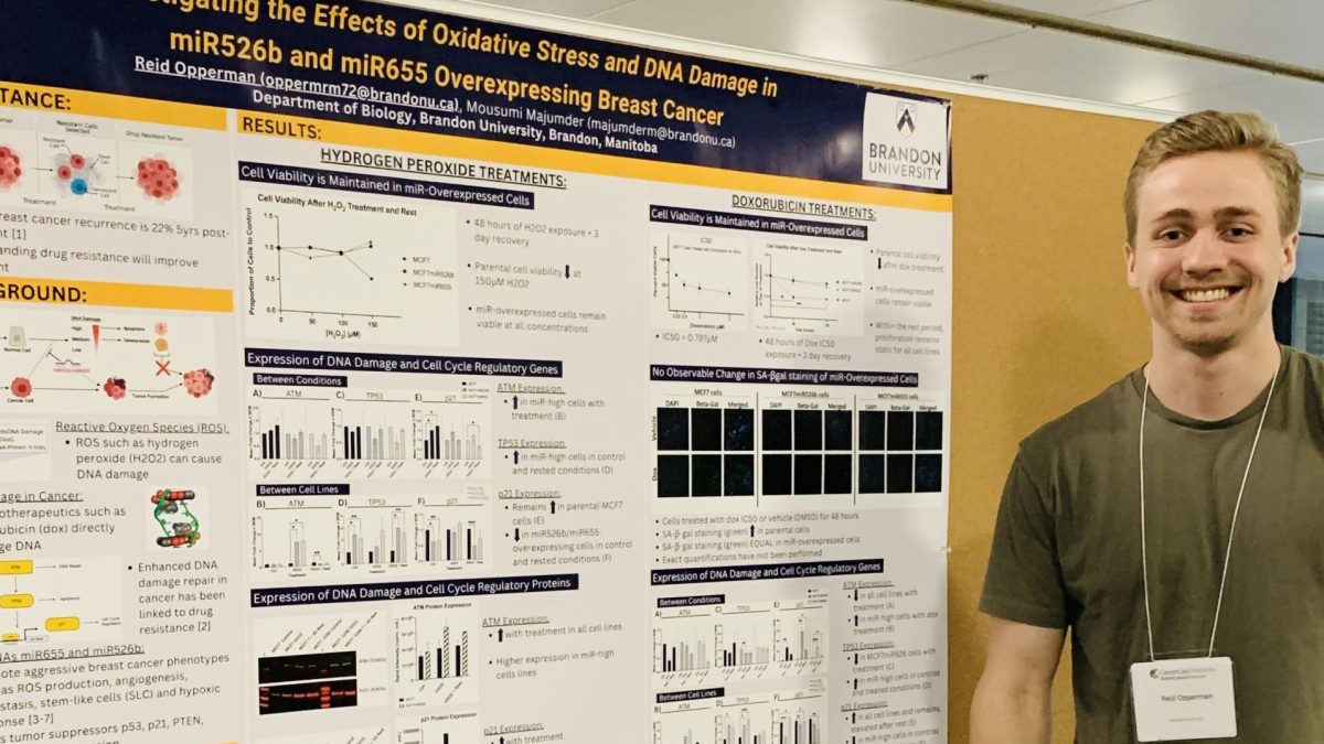 A main smiles standing next to a research poster