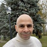 A man smiles with a tree in the background