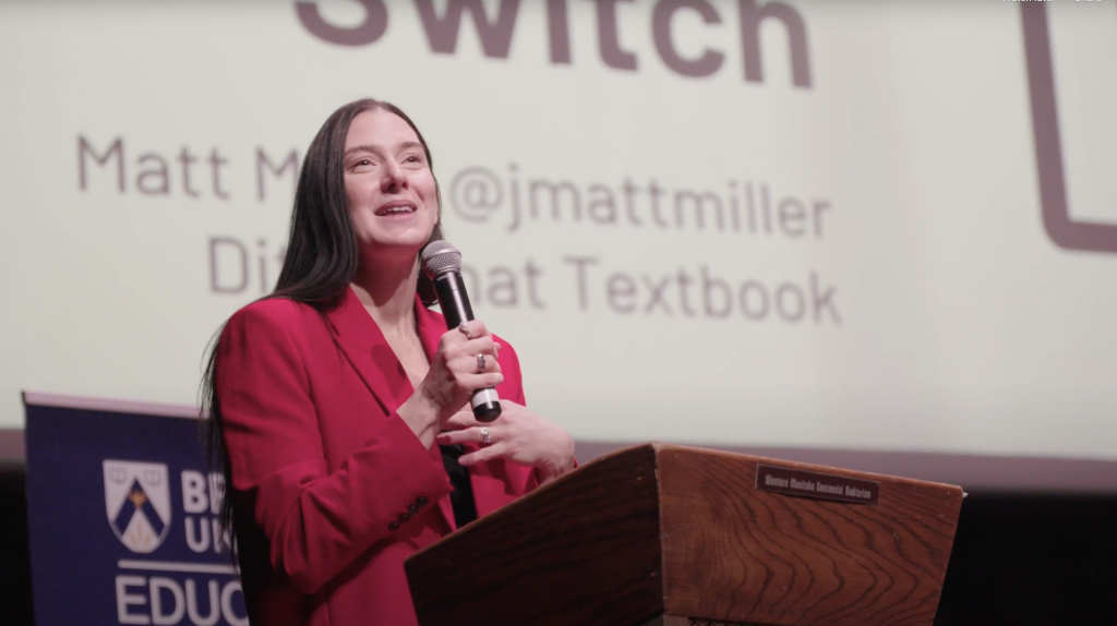 A woman holds up a microphone as she speaks at a podium.