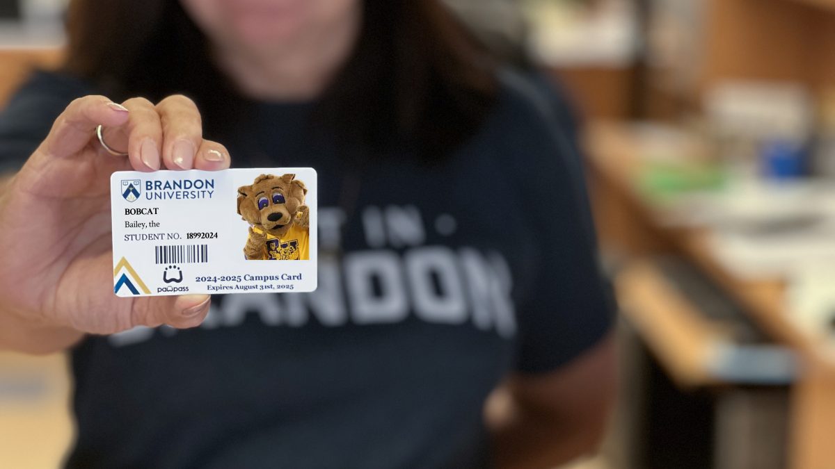 A woman holds a student ID card. The card features the university mascot, a cartoon bobcat named Bailey.