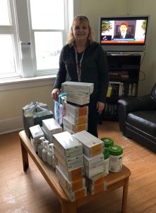 A woman stands behind a table wth several containers of medical supplies on top of it.