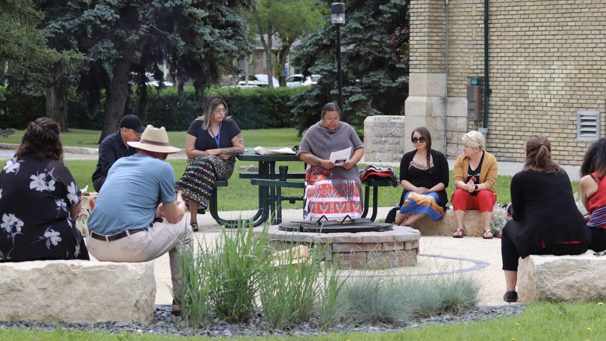 A group of people sit in a circle around a naturally landscaped area.