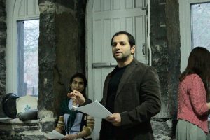 An actor reads from a script while another actor looks on from behind.