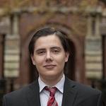 A man poses in front of a stone building