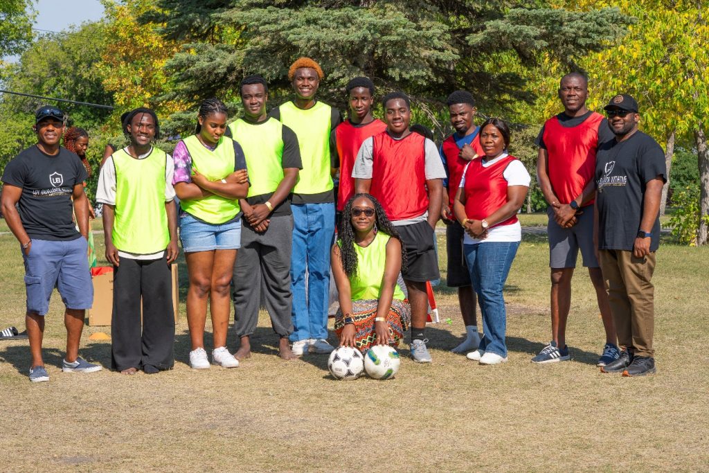 A group of people pose with two soccer balls in front of them.